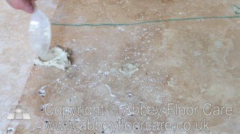 Sanded grout being applied to a small travertine hole with a spoon
